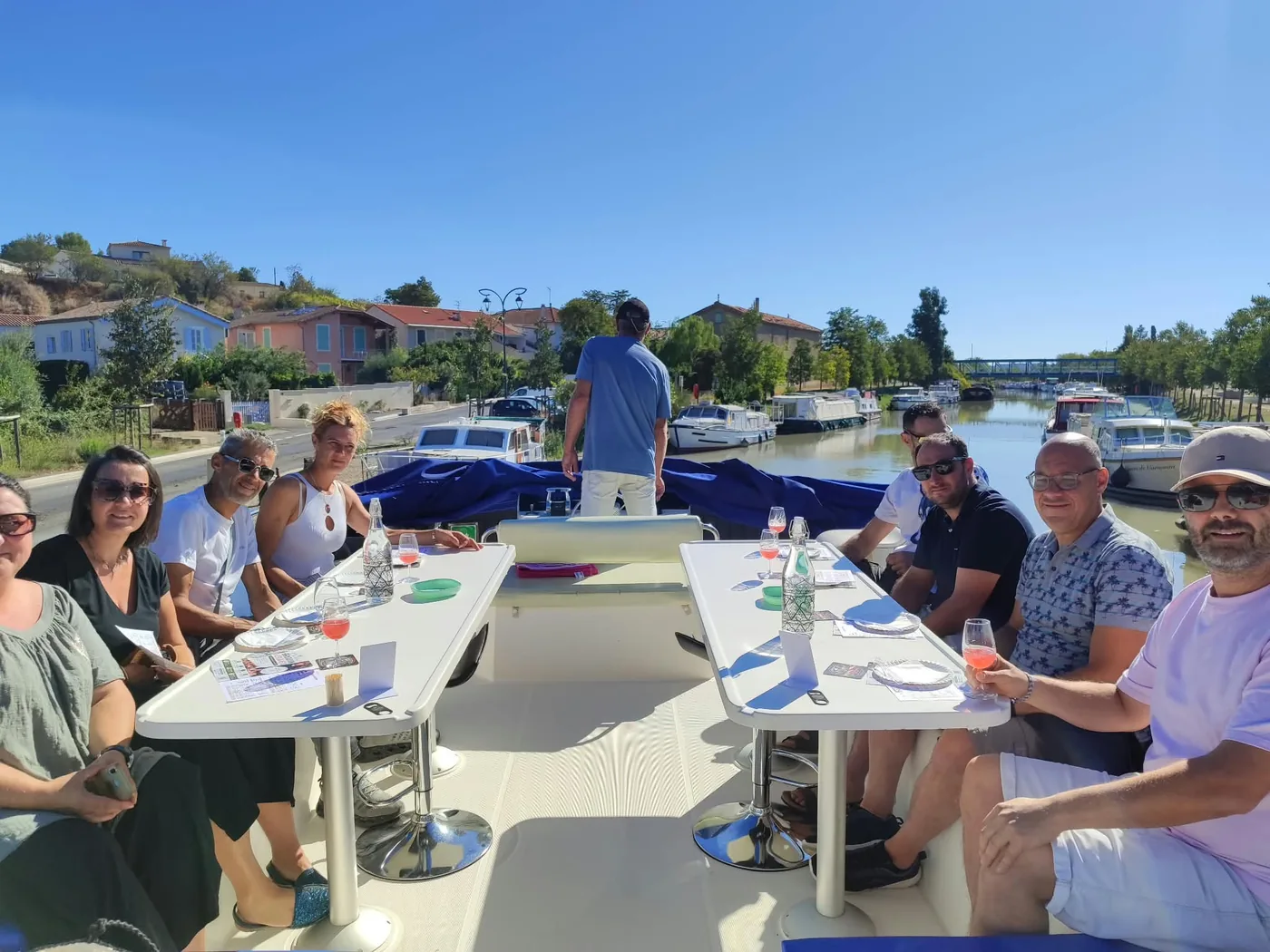 Un groupe en pleine dégustation bières et mets autour de deux tables, sur le pont d'une péniche amarrée au Canal du Midi