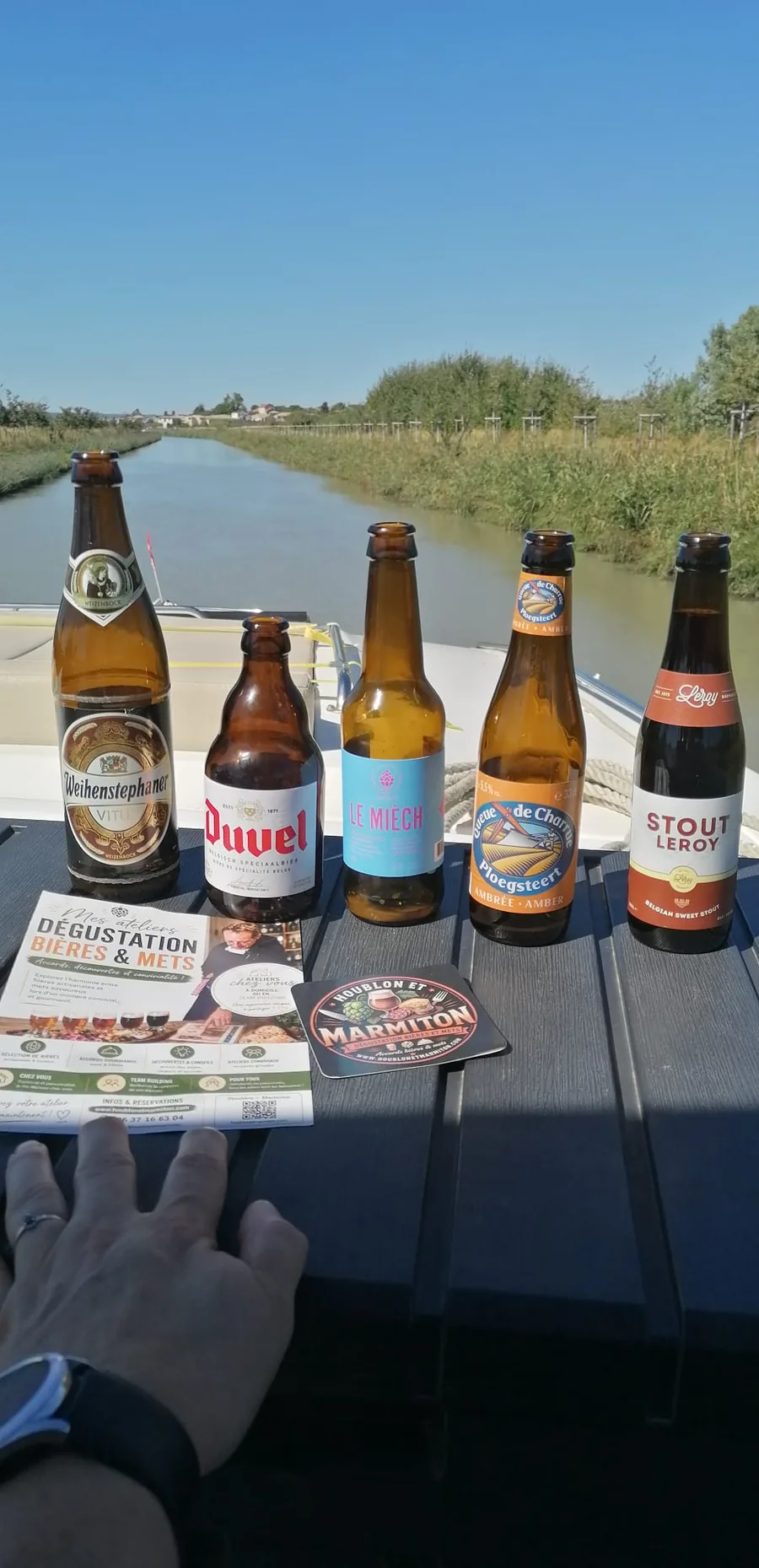 La sélection de cinq bières d'un atelier Houblon et Marmiton, avec la fiche de dégustation, devant le Canal du Midi