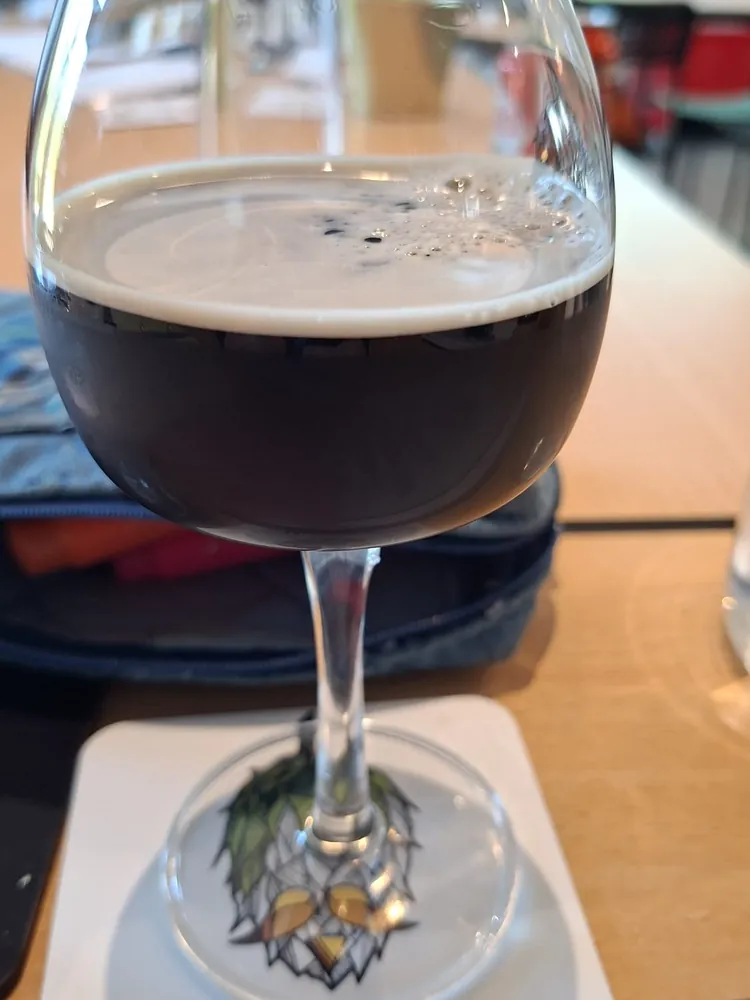 Verre de bière brune à mousse beige sur un sous-verre Hoptimalt